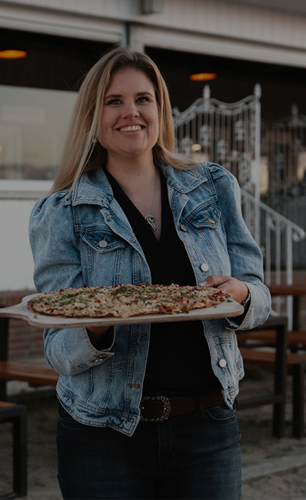 A smiling woman is holding a plate with a pizza on it.