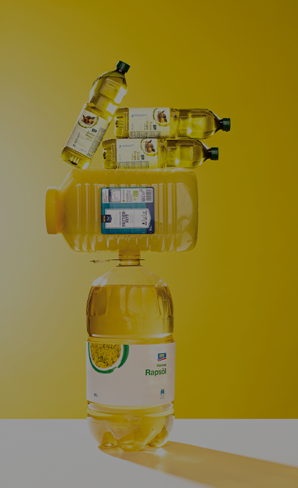 The image features a yellow background with a bottle of oil placed on top of four other bottles of oil.