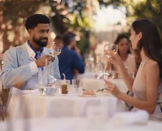 A man and a woman are sitting at a table in a restaurant, having a conversation while enjoying their meal and wine.