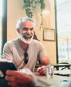 A man with a beard and mustache is sitting at a table in a restaurant, smiling and laughing.