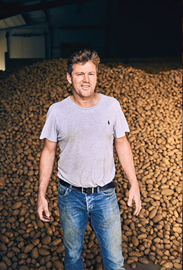 Potatoe farmer in front of a hill of potatoes in a storage hall (photo)